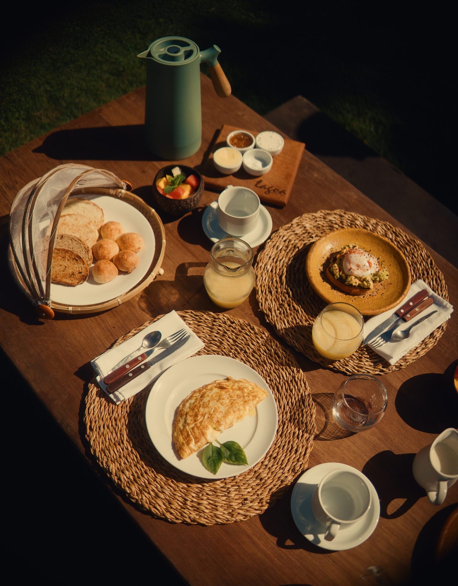 Mesa de café da manhã servida individualmente com pães, omelete, frutas e sucos
