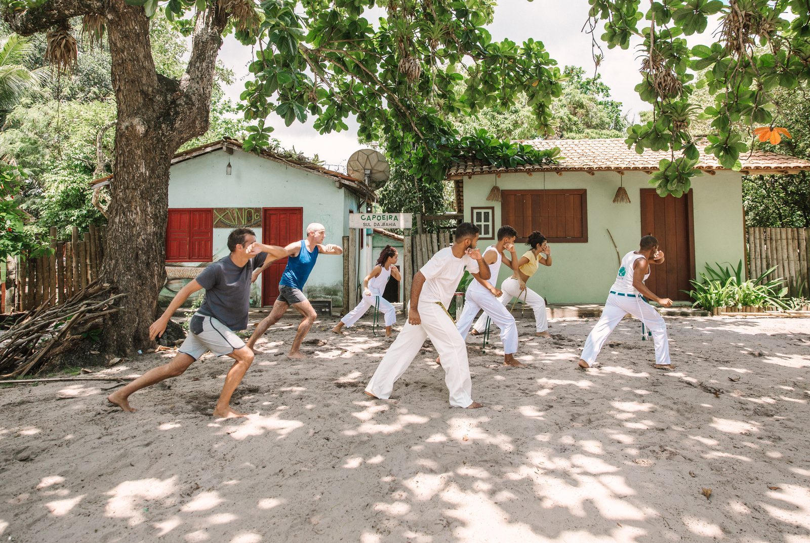Roda de capoeira na areia da vila, sob a sombra das árvores